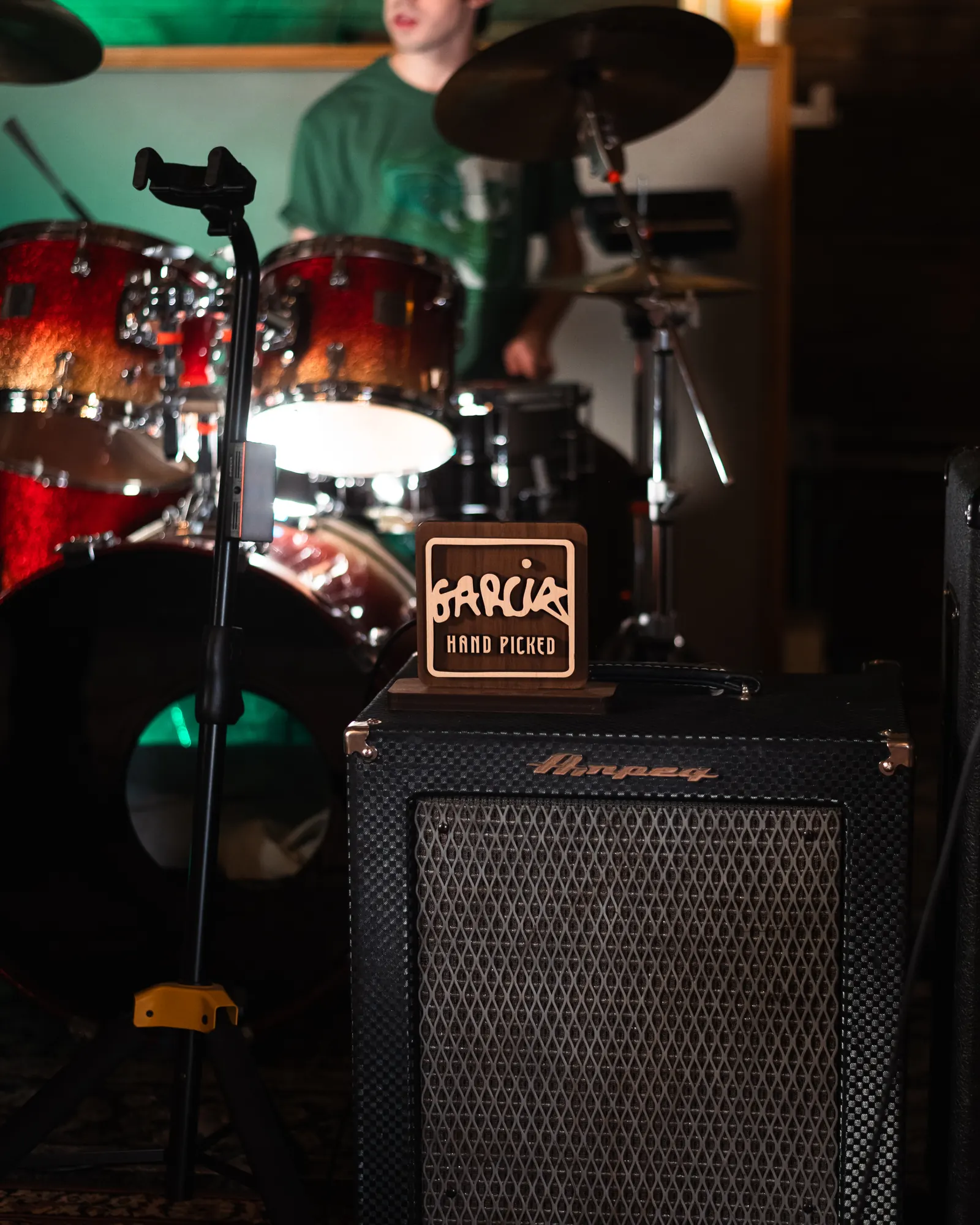 Carved Garcia Hand Picked sign lit on an Ampeg cabinet, a drum kit behind it