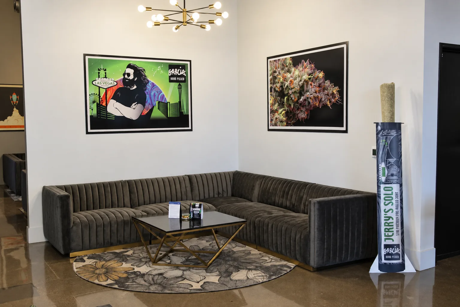Thrive dispensary lounge with the framed Las Vegas Garcia artwork on the wall and a tall Jerry's Solo pre-roll display column beside the sofa
