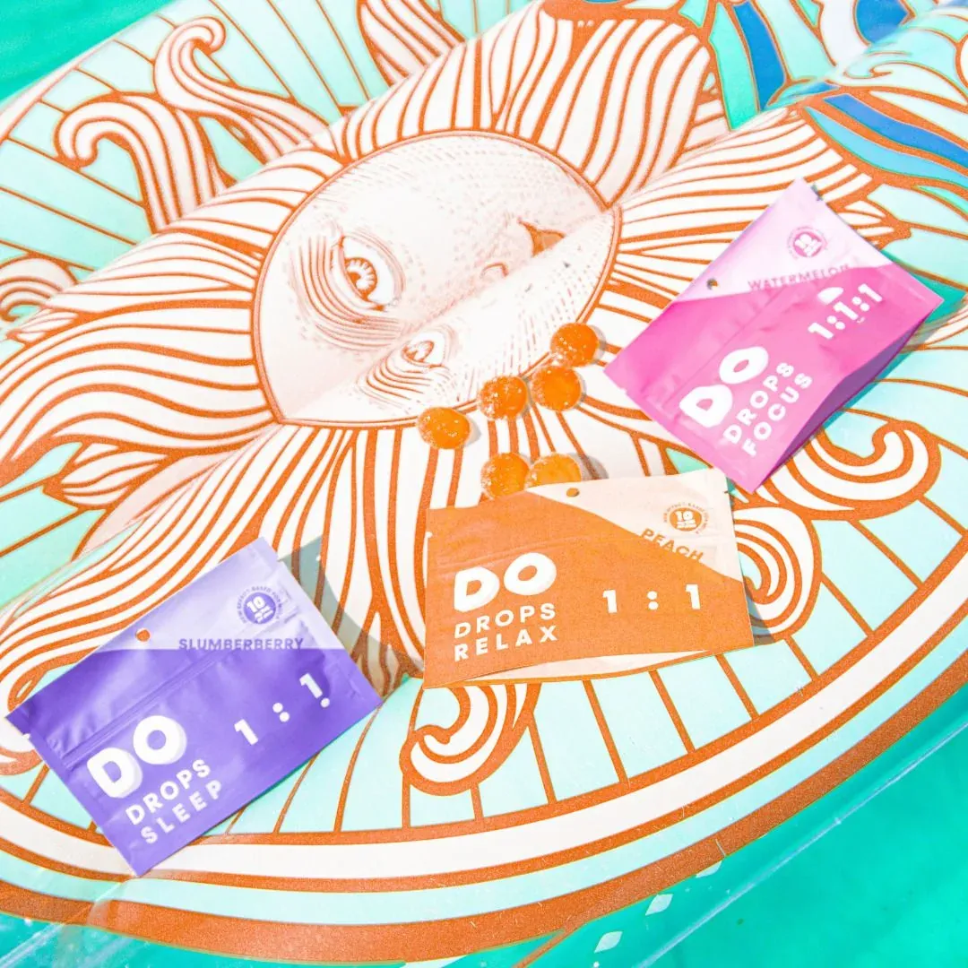 Three DO Drops pouches arranged on an illustrated orange and teal sunburst plate.